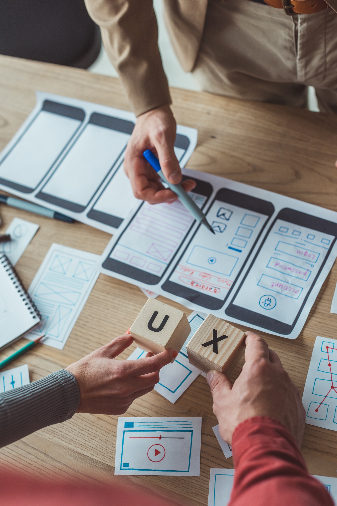 Cropped view of designers holding cubes with ux letters while working with layouts at table